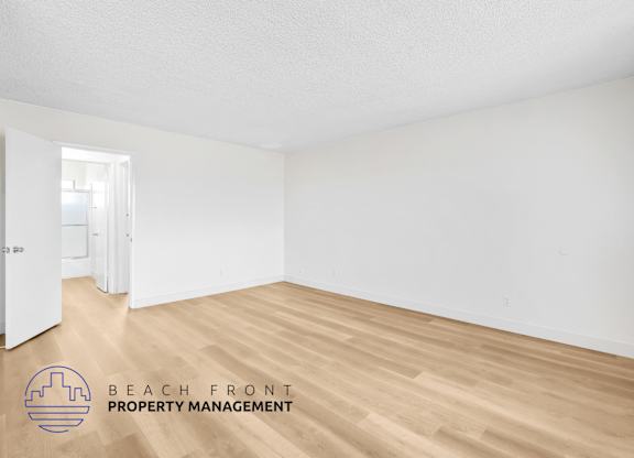 A room with wooden flooring and white walls, with a doorway leading to another room.
