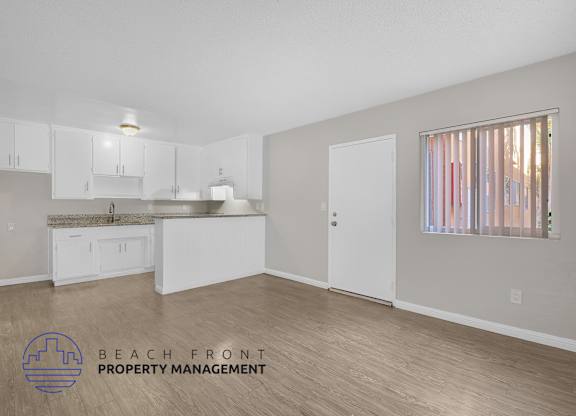 A spacious room with a kitchen area and a window with a view of the beach.