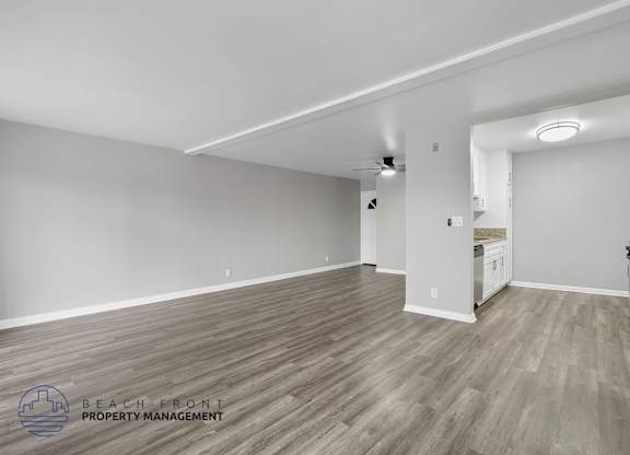 A spacious room with wooden flooring and white walls, with a logo for Beach Front Property Management in the bottom left corner.
