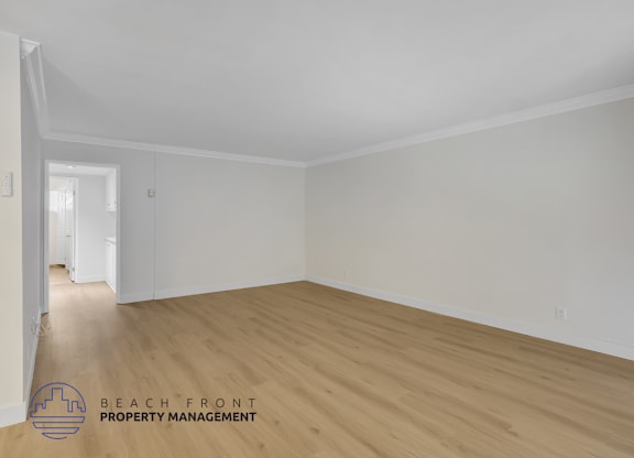 A room with wooden flooring and white walls, with a logo for Beach Front Property Management in the bottom left corner.