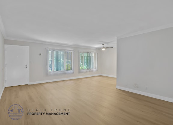 A spacious room with wooden flooring and a window with white curtains.