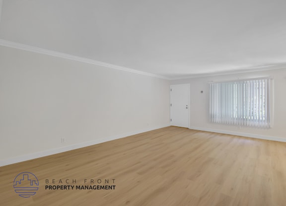 A room with wooden flooring and a window with white curtains.