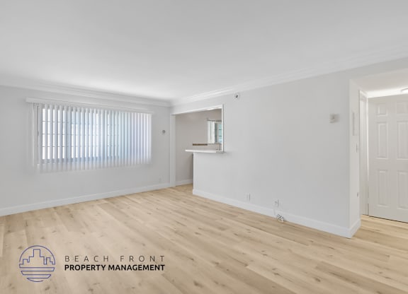 A room with wooden flooring and white walls, with a window covered by vertical blinds.