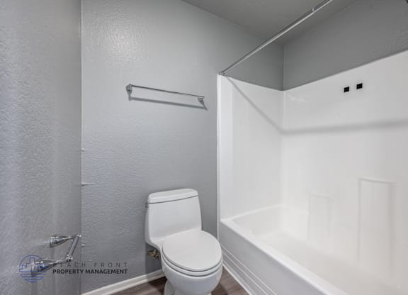 A white toilet in a small bathroom with a white bathtub.