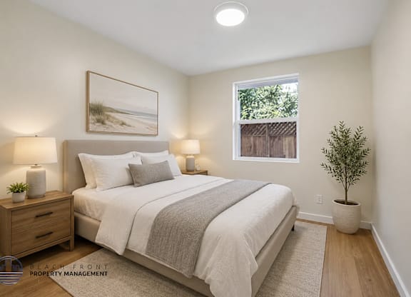 A bedroom with a large bed, two lamps, a potted plant, and a framed picture on the wall.