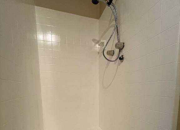 A white tiled shower with a drain in the bottom.