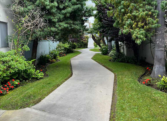 A concrete pathway leads through a landscaped area with trees and shrubs.