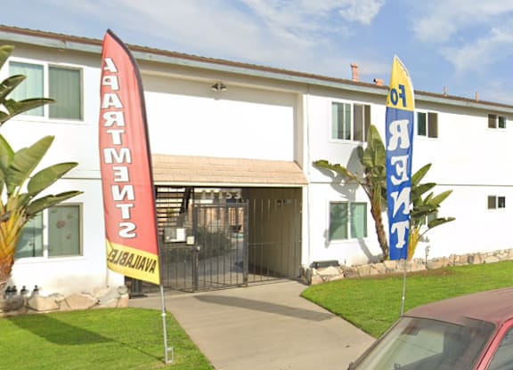 A red car is parked in front of a white building with a red and yellow sign that reads