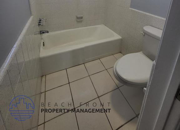 A white toilet is in a small bathroom with a white tub.