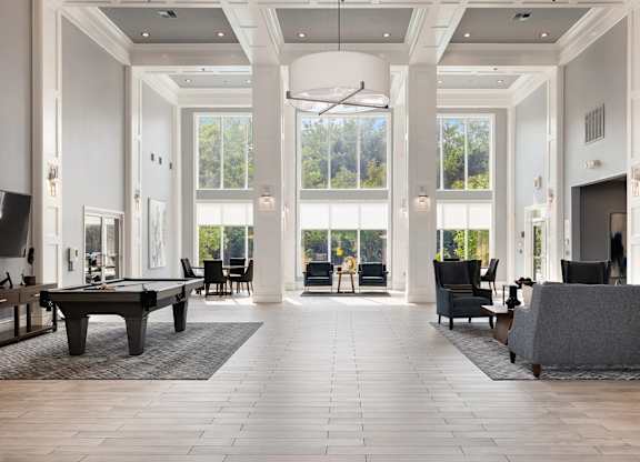 A large, open-concept living room with a pool table and a view of the trees outside the windows.