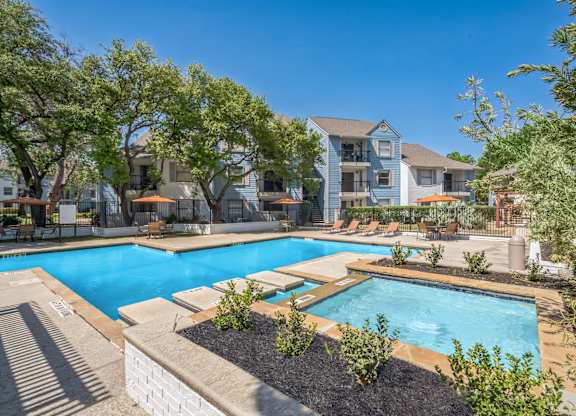 A swimming pool surrounded by trees and plants with a building in the background.