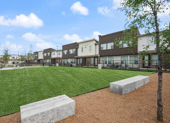 A park with a grassy area, a bench, and a tree in front of apartment buildings.