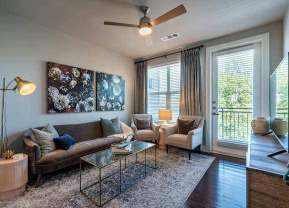 A living room with a brown couch, a glass coffee table, and a ceiling fan.