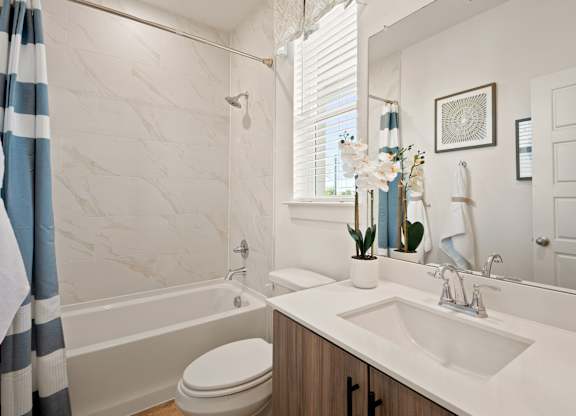 A bathroom with a white sink, toilet, and a shower with a striped shower curtain.