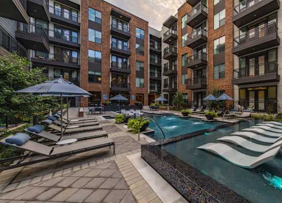 A pool surrounded by lounge chairs and umbrellas in a courtyard.