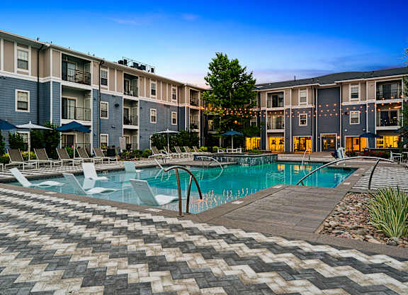 A large swimming pool surrounded by a brick patio and lounge chairs.