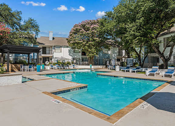 A large swimming pool surrounded by trees and lounge chairs.