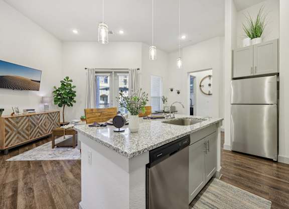 Bright view from the kitchen into a living room with eggshell paint and dark wood floors.