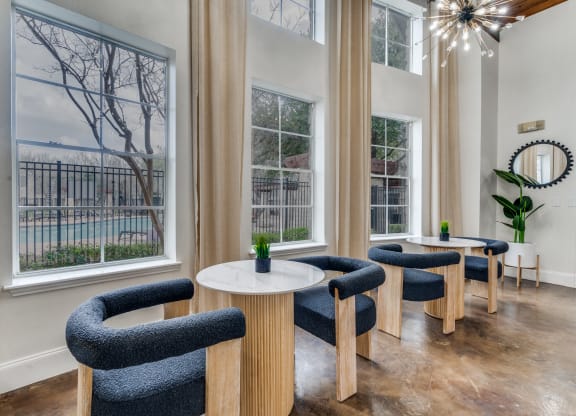 a living room with chairs and tables and large windows