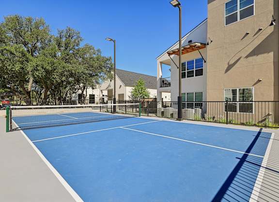 A tennis court is surrounded by a fence and a building.