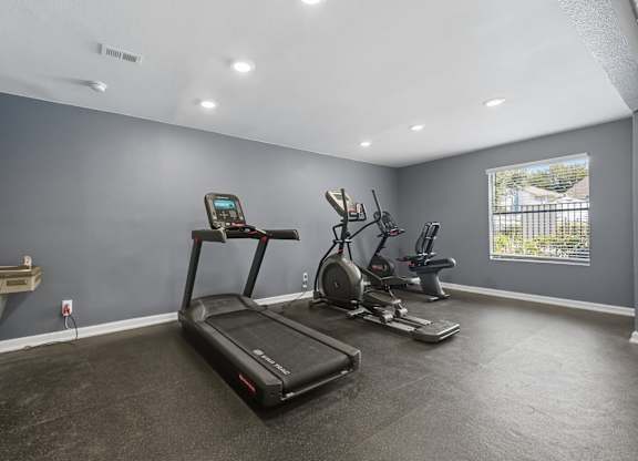 A spacious room with a treadmill, elliptical machines, and a table.
