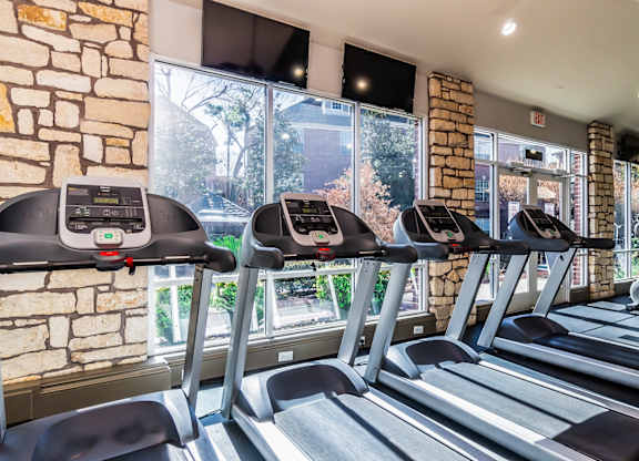 A gym with treadmills and a brick wall.