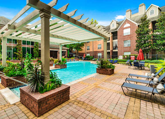 A pool area with a pergola and lounge chairs.