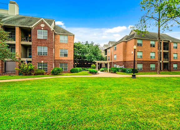 A large grassy area in front of two red brick apartment buildings.