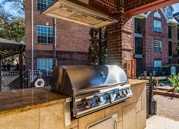 A BBQ grill is on a patio with a pool and trees in the background.