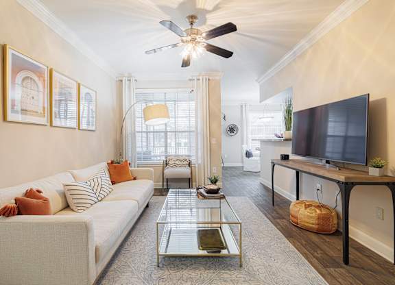 A living room with a white couch, a glass coffee table, and a television.