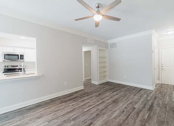 an empty living room with a ceiling fan and a kitchen
