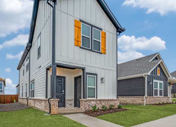 A modern house with a grey and white exterior and orange window shutters.