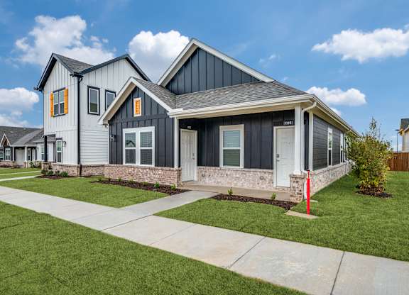 A modern house with a grey and black exterior and a red post in the front yard.