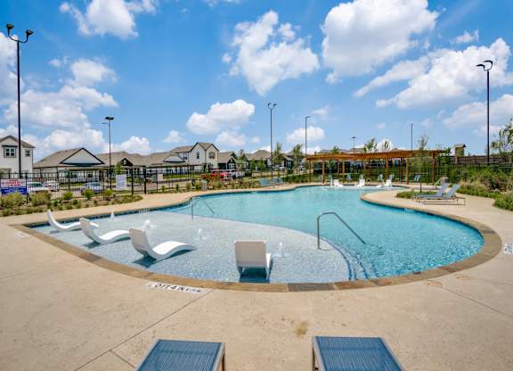 A round swimming pool with a blue tiled edge and white lounge chairs.