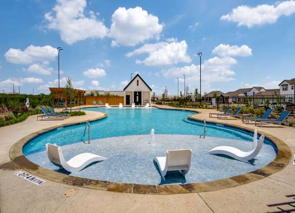 A round swimming pool with a fountain in the middle and lounge chairs around it.