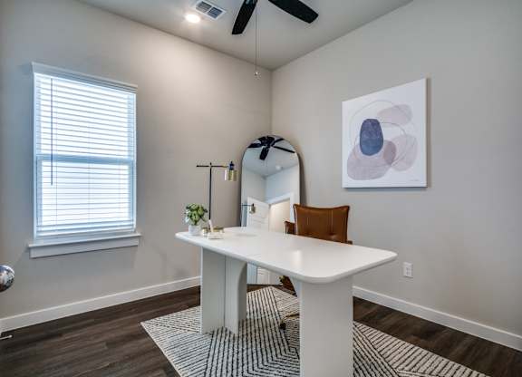 A white table with a brown chair and a mirror in a room with a ceiling fan.