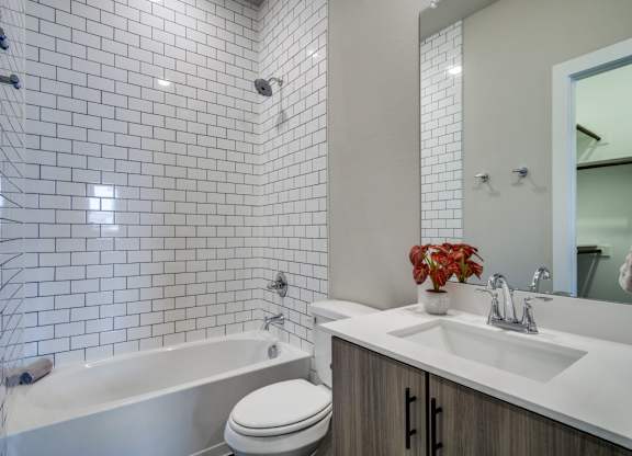 A white toilet sits next to a bathtub in a bathroom with white tiles.