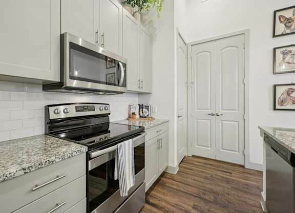 Close-up of a built-in stainless steel microwave set against light cabinetry, with a glimpse of the dark floors and bright kitchen in the background.