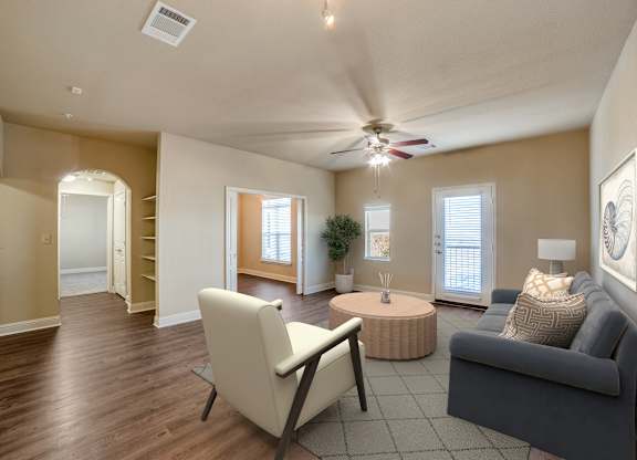 A living room with a white chair, a grey couch, and a round table with a plant on it.