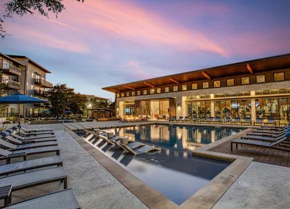 A large outdoor swimming pool with lounge chairs and a building in the background.