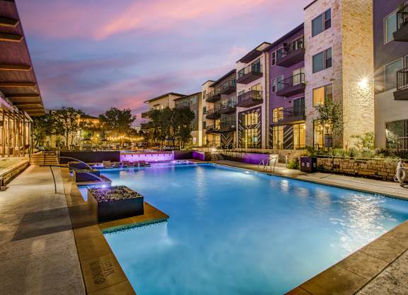 A swimming pool in front of apartment buildings at dusk.