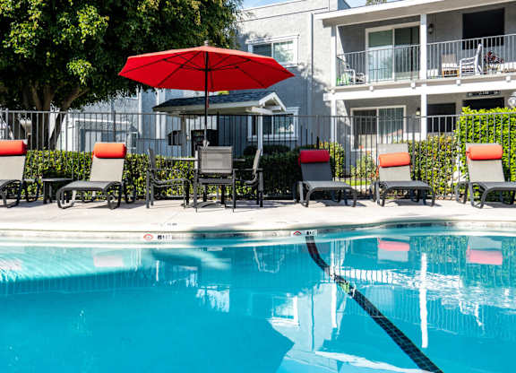 A pool with chairs and an umbrella in front of a building.