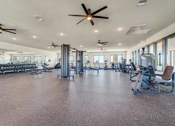 A spacious gym with a variety of equipment and a ceiling fan.