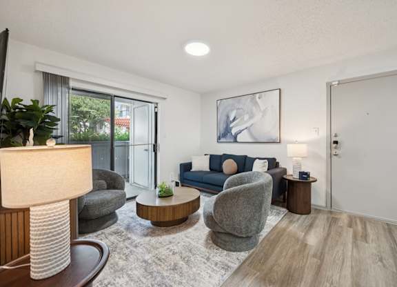 A modern living room with a grey sofa, a grey armchair, a wooden coffee table, and a white lamp.
