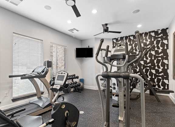 a gym with cardio machines and a tv