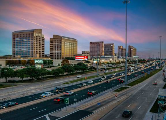 A busy highway with cars driving in both directions and tall buildings in the background.