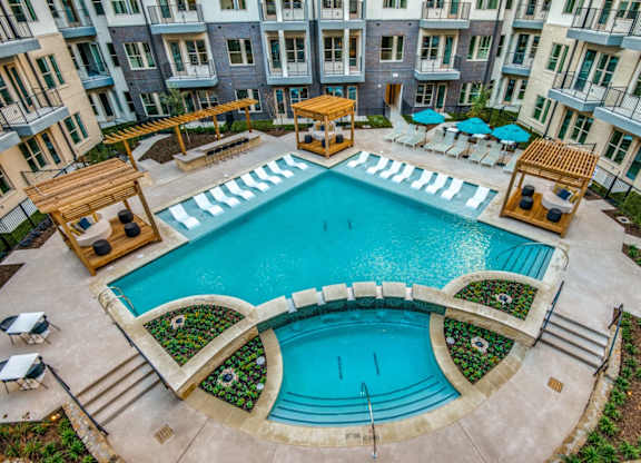 A large outdoor swimming pool surrounded by a patio area with chairs and umbrellas.
