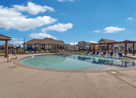 A large outdoor swimming pool surrounded by a fence and a pergola.