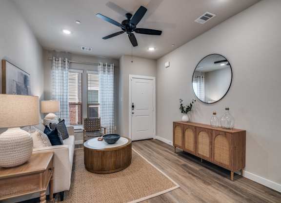 A living room with a ceiling fan, a round mirror, and a wooden cabinet.