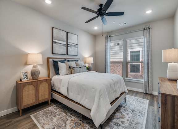 A bedroom with a bed, two lamps, and a ceiling fan.